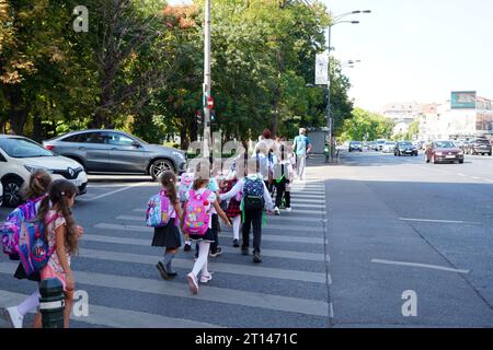 Bucharest, Romania - September 12, 2023: Elementary school children crossing street on crosswalk in a row holding hands two by two Stock Photo