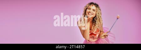 pretty joyful woman in tooth fairy costume with magic wand in hand sending kiss at camera, banner Stock Photo
