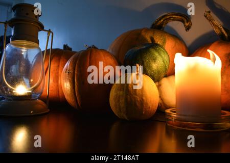 A selection of pumpkins and squashes displayed on a black table with a candle and a tea light storm lantern casting light and shadow on to them. Stock Photo