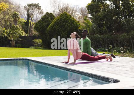 Happy diverse couple practicing yoga stretching next to swimming pool in sunny garden, copy space Stock Photo