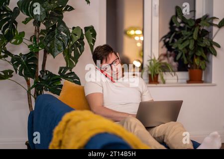 Busy man sitting on couch with laptop. Serious guy with glasses talking on phone, focused on work Stock Photo