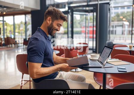 Smiling male architect is making notes during work on laptop in modern coworking space Stock Photo
