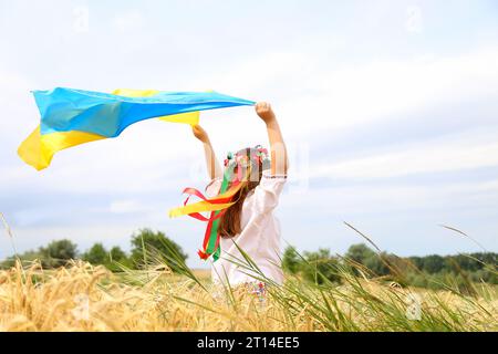 Happy Ukrainian girl carries fluttering blue and yellow flag of Ukraine against blue sky and sea background. Ukrainian flag is a symbol of independenc Stock Photo