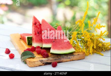 Watermelon pieces, raspberries, mint leaves and yellow flowers on a cutting board. Stock Photo