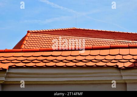 new red brown beavertailed sloped clay tile Mansard roof. ridge tile. closeup detail. modern roof construction materials. stucco elevation. blue sky Stock Photo