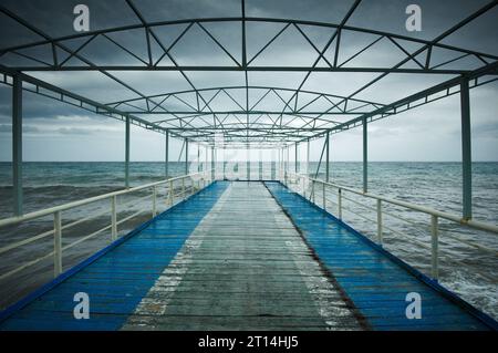Old wooden jetty, pier, during storm on the sea. Dramatic sky with dark, heavy clouds. Stock Photo