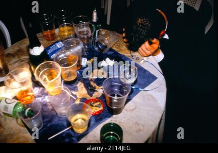 1990s UK a drunk student holds his head and rests it on a table covered in empty and half full plastic glasses of wine and beer at the end of the year annual summer May Ball. Cirencester Royal Agricultural College, Cirencester Gloucestershire, England, May 1995. HOMER SYKES Stock Photo