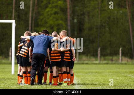 Group of school boys huddling united in soccer team before tournament football match. Boys in sports uniforms standing in a circle with coach Stock Photo