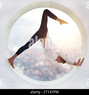 Beautiful sporty fit yogi woman practices yoga asana eka pada Adho Mukha Shvanasana One Leg Downward Dog pose in a round window with a view of the cit Stock Photo