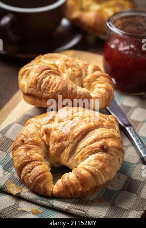 Two croissants with strawberry preserves and cup of coffee on rustic wooden table Stock Photo