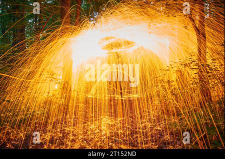 Burning steel wool spinned in the forest. Showers of glowing sparks from spinning steel wool at night. Stock Photo