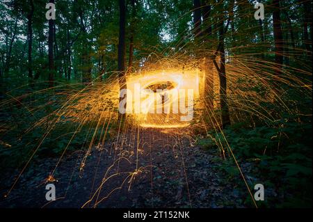 Burning steel wool spinned in the forest. Showers of glowing sparks from spinning steel wool at night. Stock Photo