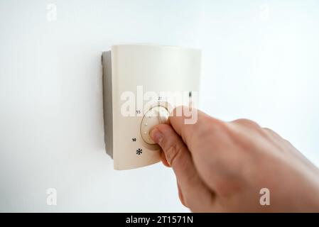 Man turning down heating thermostat to save money. Stock Photo