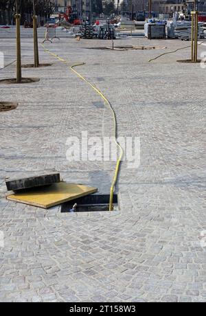 long hose inside an open manhole in cobblestone street Stock Photo