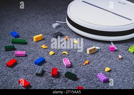 A robot vacuum cleaner cleans children's toys on the floor. Carpet and laminate cleaning. Assembling cubes with a robot vacuum cleaner.. Stock Photo