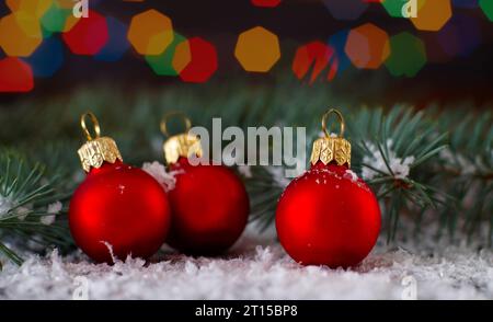 Three Red balls over blurred lights background with fir branch. Christmas and New Year Decoration. Selective focus. Stock Photo