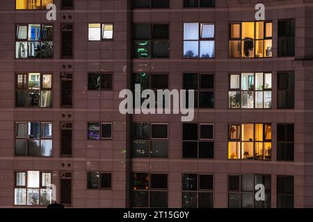An apartment where houses with the same spatial structure are stacked like tiles. After sunset, lights turn on in the windows, showing different color Stock Photo