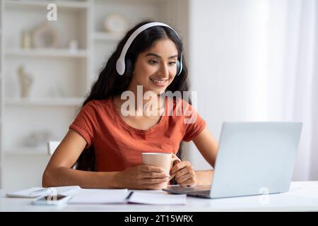 Smiling young indian woman in wireless headphones sitting at desk Stock Photo