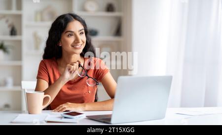Beautiful young indian woman sitting at desk, working on laptop Stock Photo