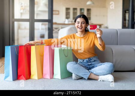 Young Indian Woman Sitting Next To Shopping Bags And Holding Credit Card Stock Photo