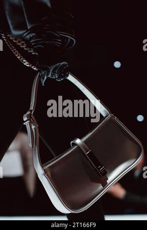 A female hand in a black leather glove holding a classic leather silver handbag. Vertical fashion shot Stock Photo