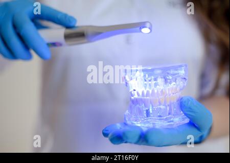 Photopolymer lamp Doctor Fairy with a glowing blue lamp in a white medical suit Dentist treatment of teeth prosthetics put fillings treat gums caries beautiful woman on white background. studio ad Stock Photo