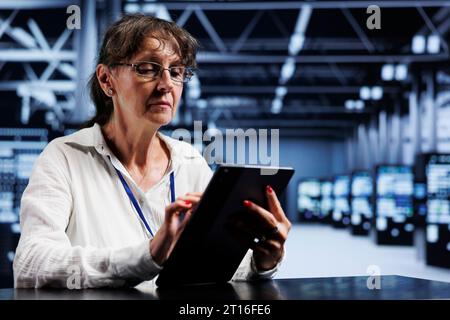 Senescent system administrator using tablet to assess server cybersecurity bugs arising due to unsecured network connections. Skilled mechanic ensuring data center is impenetrable by ddos attacks Stock Photo
