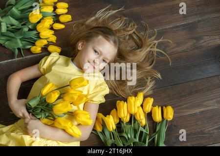 A young girl in a yellow dress lies among yellow tulips. View from above. Stock Photo