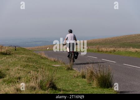 Dartmoor, Devon, Englaand, UK. 04.09.2023.  Man cycling on  an empty road  in Dartmoor national park in Devon, UK Stock Photo