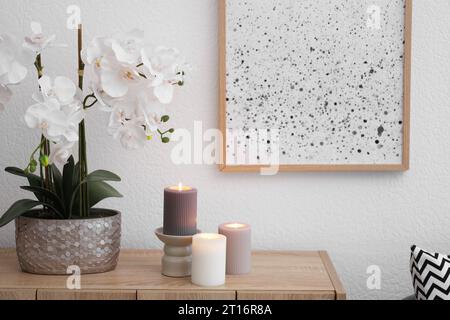 Beautiful orchid flowers and burning candles on wooden chest of drawers indoors Stock Photo
