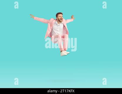 Funny excited man wearing stylish pink suit jumping isolated on studio blue background. Stock Photo