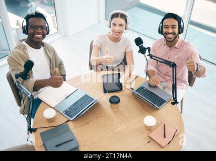 Thumbs up, people in radio and hosting talk show, broadcast and content creation with people in portrait. Headphones, laptop and mic, podcast success Stock Photo