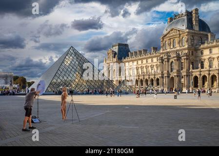 A female model and photographer in Napoleon Courtyard next to the glass Louvre Pyramid and Louvre Museum, Paris, France. Stock Photo