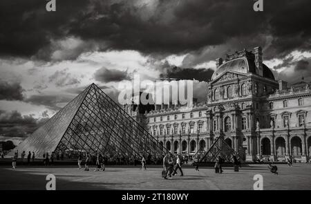 Tourists in Napoleon Courtyard next to the glass Louvre Pyramid and Louvre Museum, Paris, France. Stock Photo