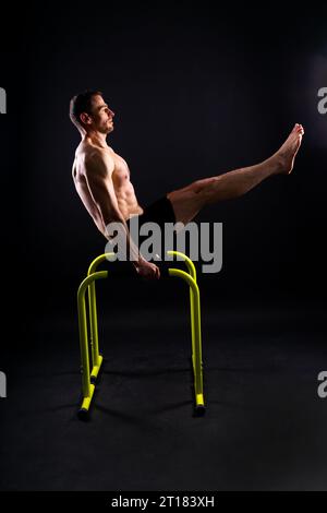 Front and side view photo of an strong young man exercising on parallel bars in studio. Stock Photo