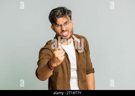 Quarrel. Displeased aggressive unhappy Indian young man gesturing hands with irritation and displeasure, blaming scolding for failure, asking why this happened. Arabian guy isolated on gray background Stock Photo