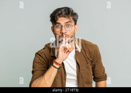 Shh be quiet please. Indian young man presses index finger to lips makes silence gesture sign do not tells secret, stop talk gossip, confidential privacy. Arabian guy isolated on gray background Stock Photo