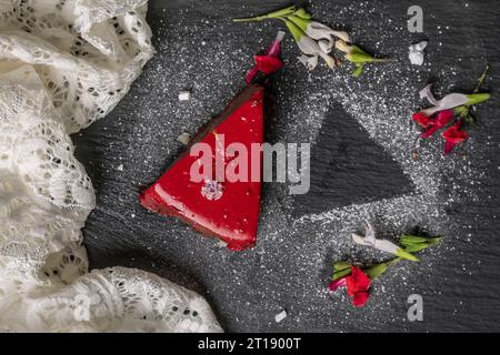 Top view of a slice of cake covered in red icing, decorated with white and red flowers and icing sugar Stock Photo