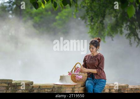 Woman sitting on a brick wall with a basket filled with  flowers, Thailand Stock Photo