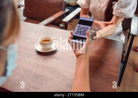 Woman scanning a QR code to make a payment in a coffee shop Stock Photo