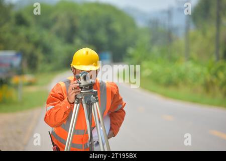 Surveyor standing in a the middle of a road using a theodolite, Thailand Stock Photo