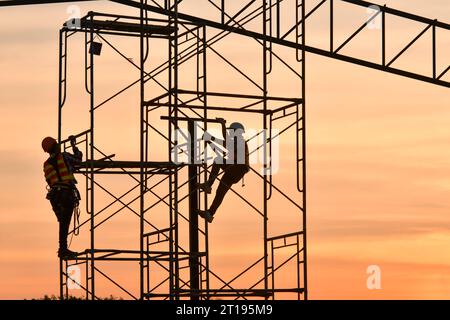 Silhouette of two construction works climbing on scaffolding, Thailand Stock Photo