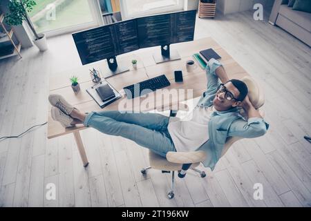 Photo of handsome professional it specialist having rest end buy day put legs on desktop relaxing geek after fixing bugs indoors workshop Stock Photo