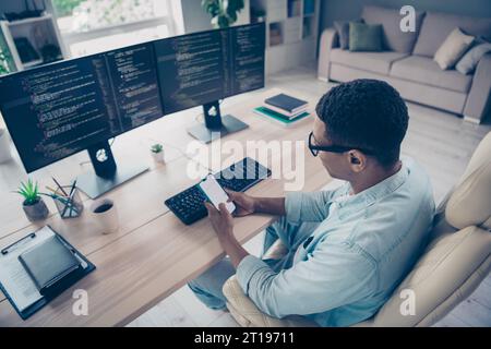 Side view photo of young program developer creating mobile games holding smartphone texting email his colleagues sitting workspace indoors Stock Photo