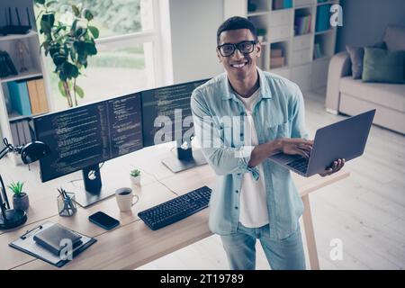Photo of successful handsome young web designer content editor holding netbook distant worker doing python code at home indoors workspace Stock Photo