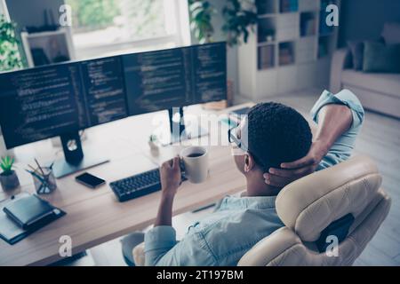 Rear back view photo of holding cup fresh coffee it specialist control cyber security his code managing juniors job indoors workplace Stock Photo