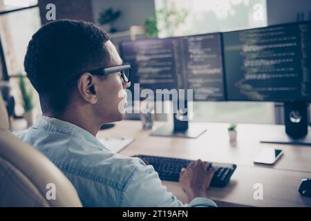 Rear photo of smart skilled young man worker qa engineer testing open data code typing keyboard looking computer monitors in office room Stock Photo