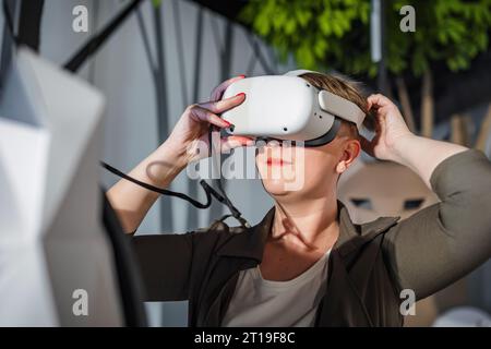 Young woman wearing virtual reality headset enjoying VR experience thrilled pointing around her during natural history museum visit. Stock Photo