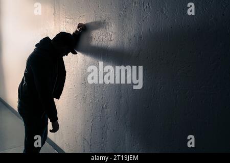Drunk, intoxicated man against wall. Alcohol problem, drug addiction or overdose concept. Nauseous, vomit on street. Young dizzy person in dark alley. Stock Photo