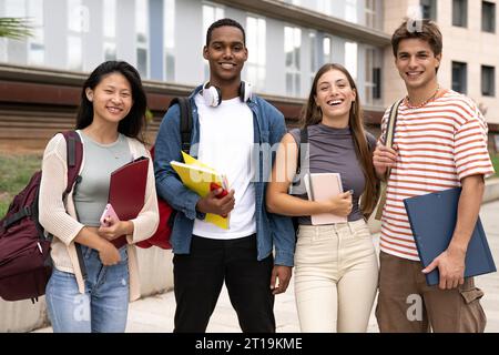 Handsome satisfied student holding a notebook looking at camera leaning against a glass wall.Confident and happy woman standing outside with files on Stock Photo